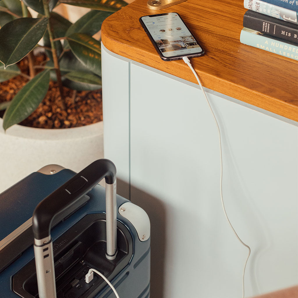 Frame carry-on in navy blue with spare battery charging an iPhone.