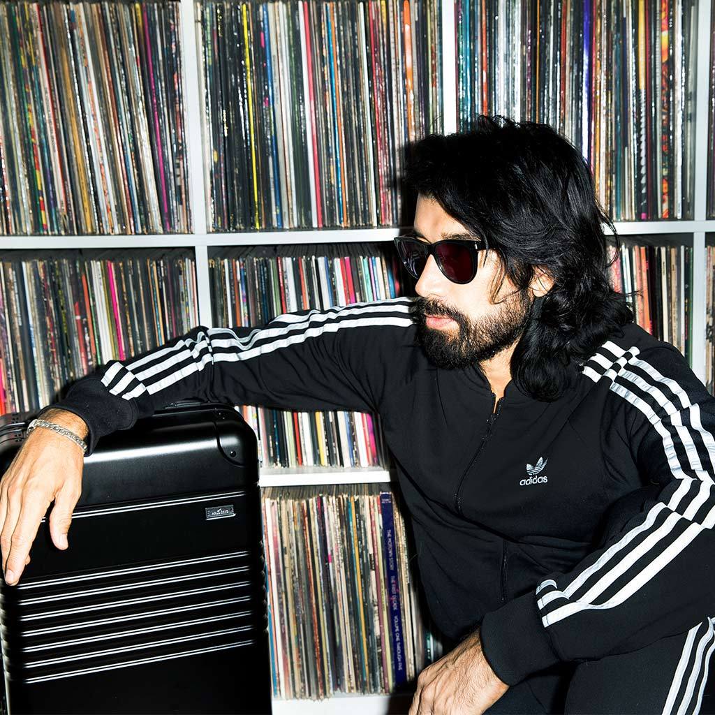 Myles Hendrik posing with his frame carry-on black in front of a wall of vinyl records.