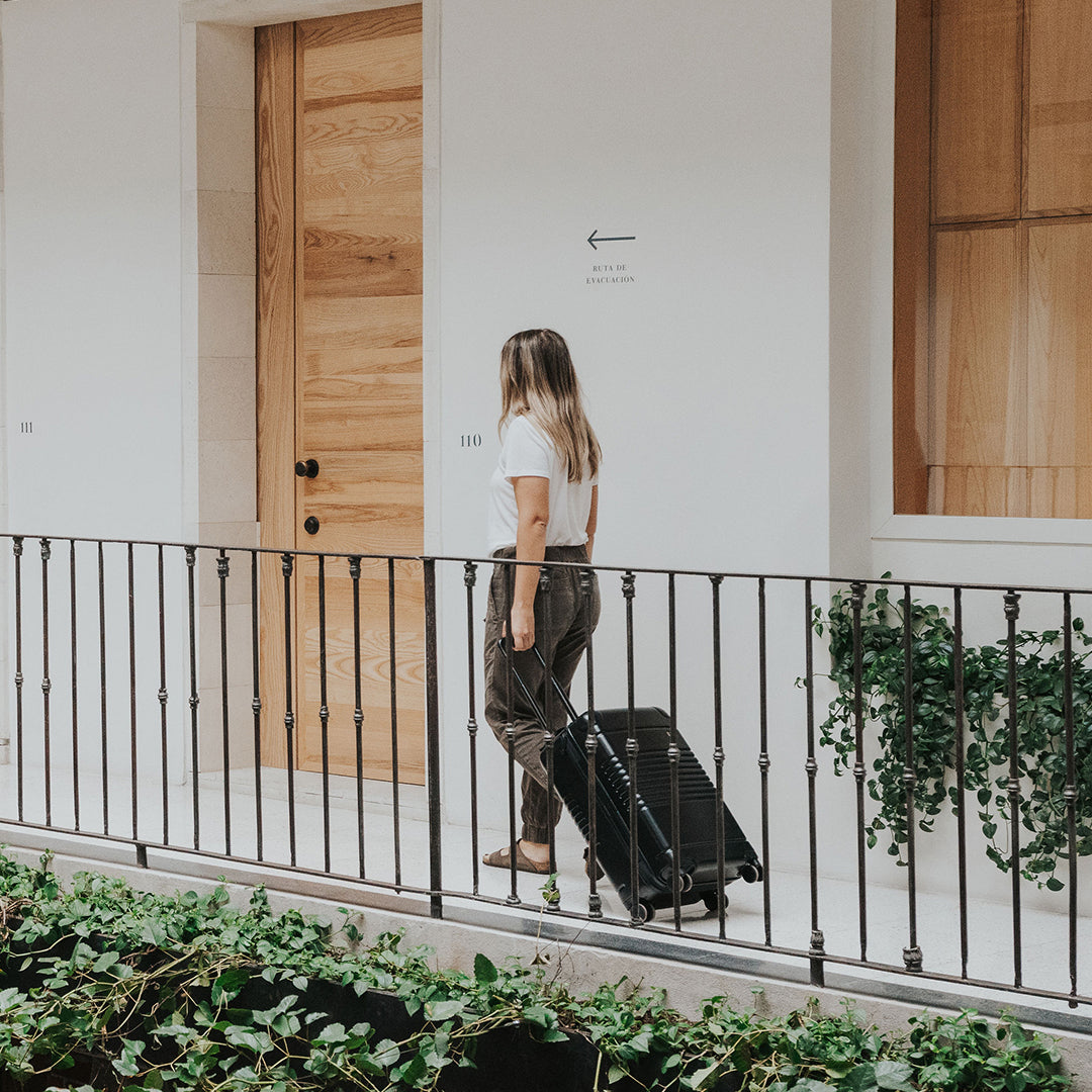 A woman with an Arlo Skye Zipper Carry-On in Black walking through a corridor of a hotel in Mexico City.