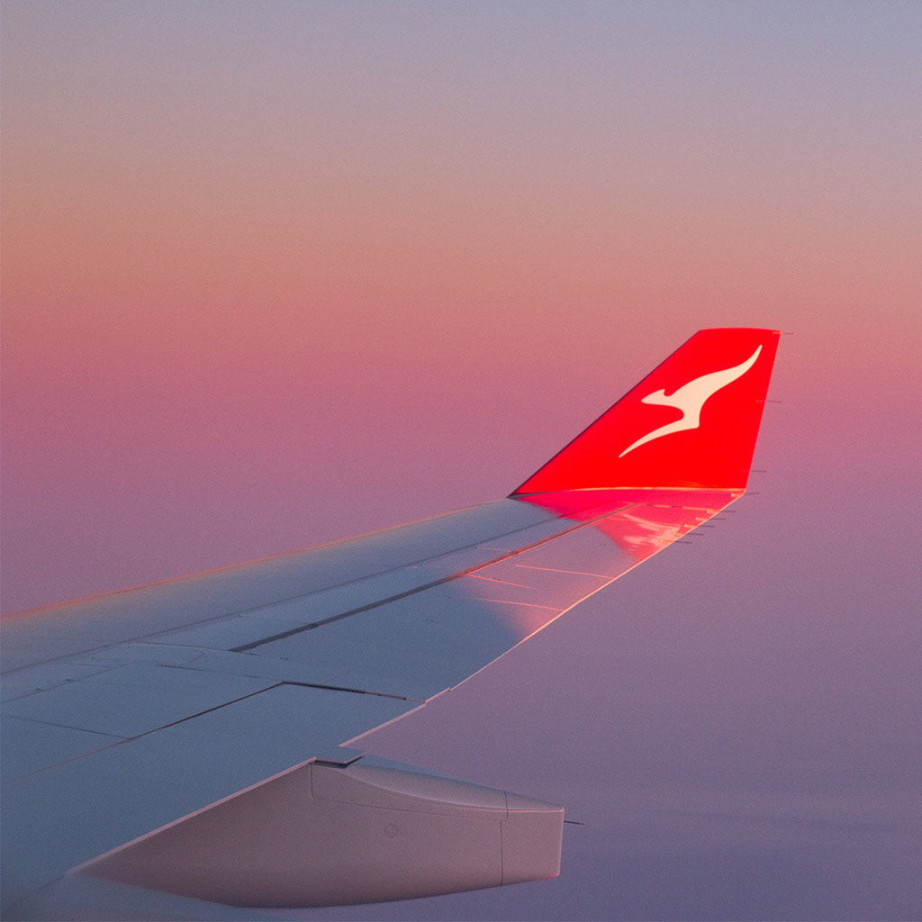 The wing of Qantas Airlines in cruising altitude with clouds below.