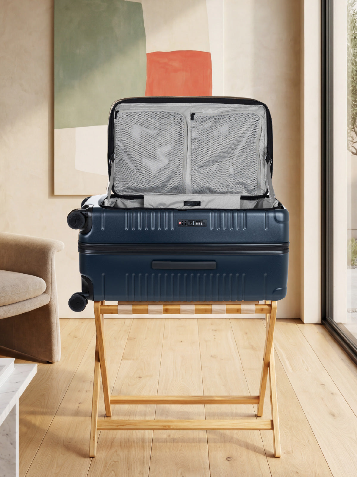 navy color trunk resting horizontally on a wooden rack with its lid open, showing the side lock mechanism and two mesh interior compartments on the upright lid