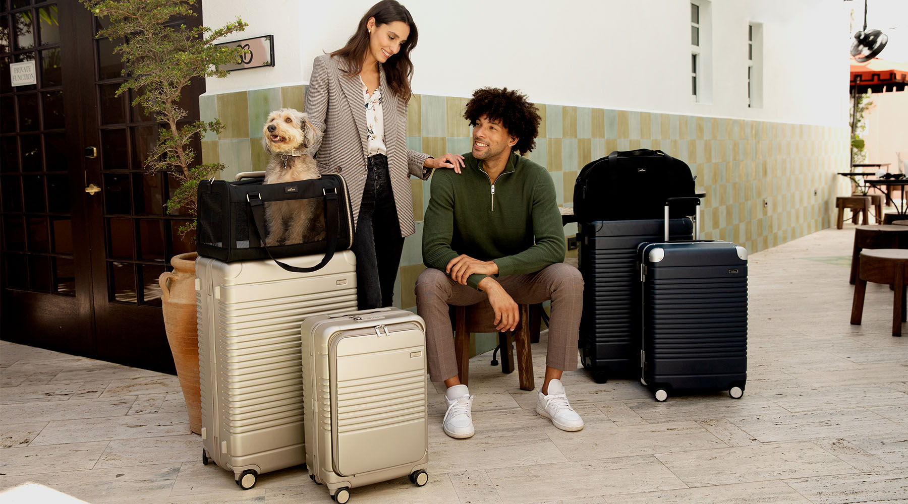 female and male model surrounded by four suitcases, a weekender and dog carrier with small dog inside.