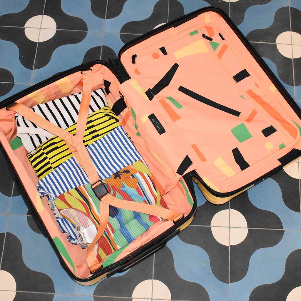 arlo skye collab with dusen carry-on is open flat on the ground with interior print showing as well as some clothes packed.