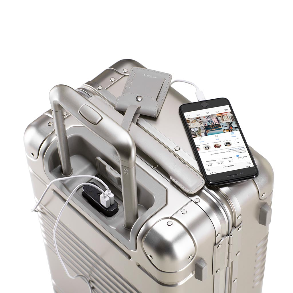 Top down view of the frame carry-on max in champagne aluminum edition showing a phone being charged by the integrated powerbank located between the telescopic handles.