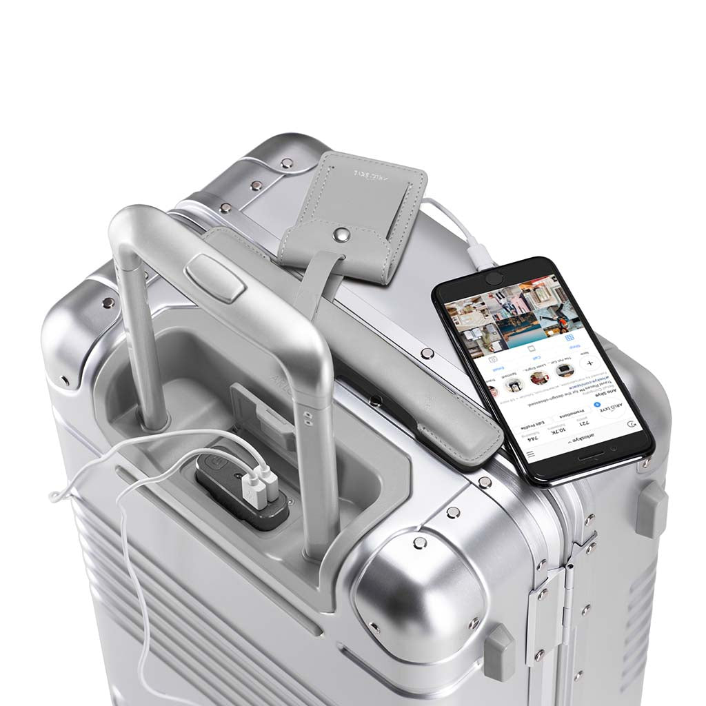 Top down view of the frame carry-on max in silver aluminum edition showing a phone being charged by the integrated powerbank located between the telescopic handles.